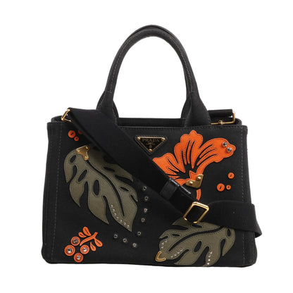 Prada Canapa Hawaii 2Way handbag in black canvas with orange and green tropical leaf and floral appliqués, gold-tone hardware, and black shoulder strap.