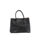 Front view of Prada Cuir black Saffiano leather handbag with twin rounded handles, red edging and a gold-tone triangular Prada logo.