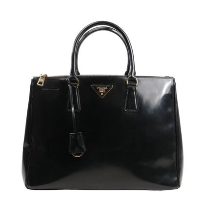 Prada Galleria 2Way handbag in black Saffiano Lux smooth leather, featuring dual rolled top handles, gold-tone hardware, zip closure, signature triangle logo plaque, and a hanging leather clochette.