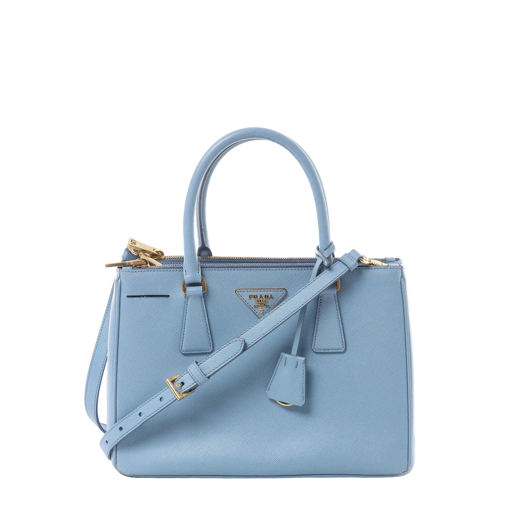 Front view of Prada Galleria handbag in light blue Saffiano leather with double top handles, gold-tone Prada triangle logo, zip-top closure, and matching shoulder strap.
