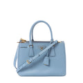 Front view of Prada Galleria handbag in light blue Saffiano leather with double top handles, gold-tone Prada triangle logo, zip-top closure, and matching shoulder strap.