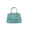 Front view of a light blue Prada Promenade Saffiano leather handbag with twin top handles, gold-tone hardware and a triangular Prada logo.