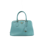 Front view of a light blue Prada Promenade Saffiano leather handbag with twin top handles, gold-tone hardware and a triangular Prada logo.
