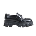 Pair of PRADA Spazzolato black leather Monolith loafers with pointy toe, chunky 55mm rubber sole, and signature silver triangle logo plaque on the strap, size 38.5 EU, photographed on a white background.