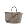 Prada Vitello Daino gray pebbled leather handbag with gold-tone Prada logo, top handles, and an adjustable shoulder strap on a white background.