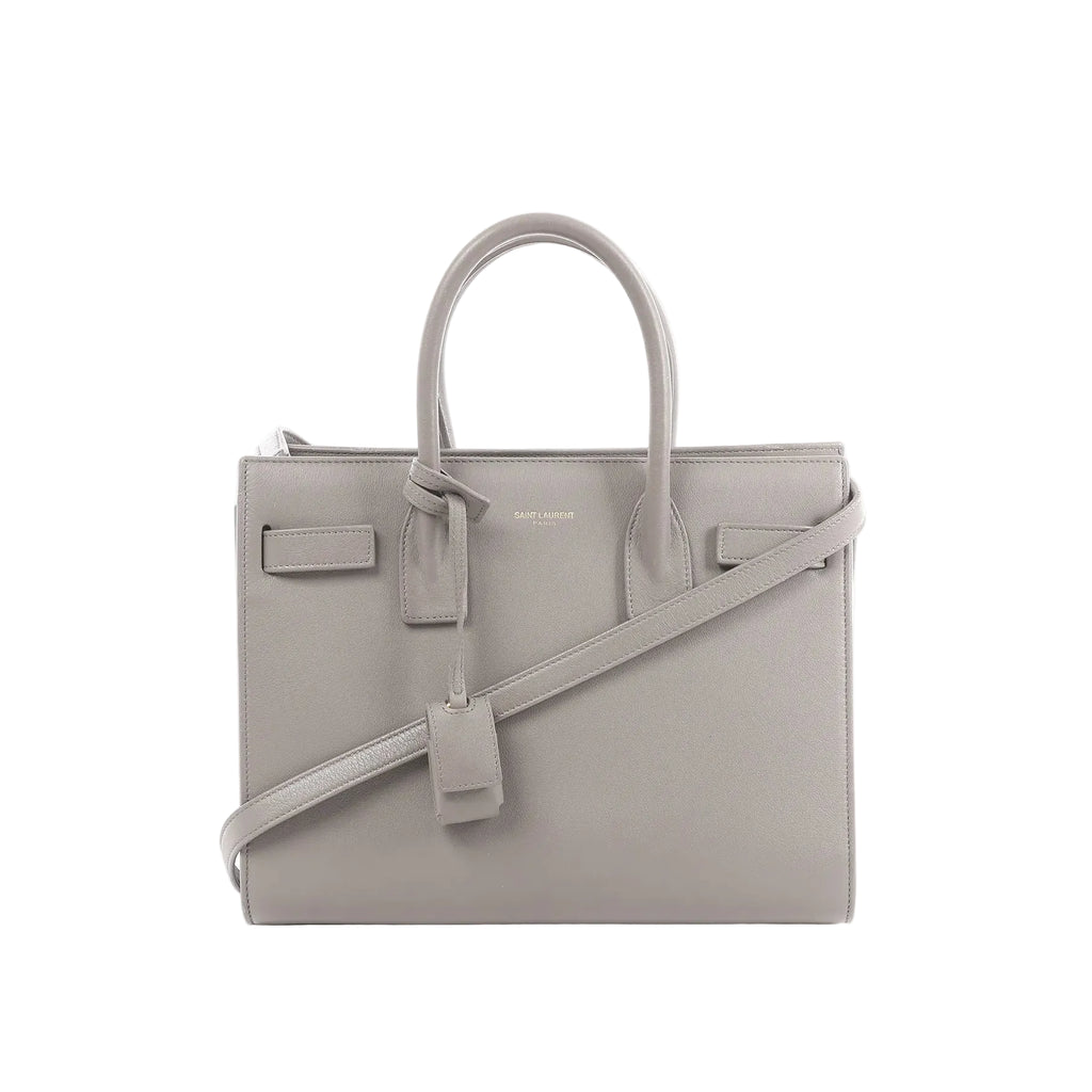 Gray Saint Laurent Baby Sac de Jour leather handbag with double top handles, detachable shoulder strap, embossed logo, and hanging leather clochette.