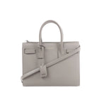 Gray Saint Laurent Baby Sac de Jour leather handbag with double top handles, detachable shoulder strap, embossed logo, and hanging leather clochette.