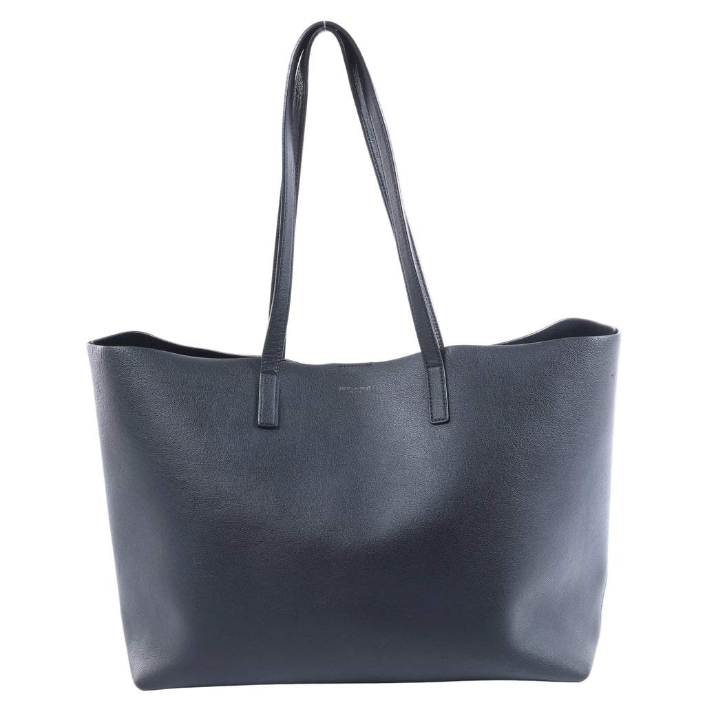 Black Saint Laurent leather tote bag with long shoulder straps, open-top silhouette and subtle gold-tone logo lettering on the front.
