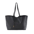 Gray Saint Laurent Sac Shopping leather tote with black shoulder straps and a gold-tone YSL charm, shown from the front on a light background.