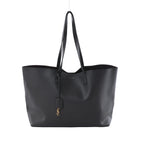 Gray Saint Laurent Sac Shopping leather tote with black shoulder straps and a gold-tone YSL charm, shown from the front on a light background.