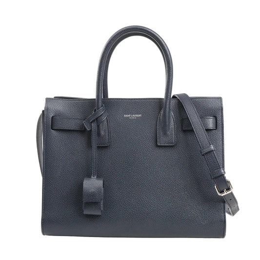 Saint Laurent Sac de Jour Baby 2Way handbag in navy blue grained leather featuring dual top handles, adjustable shoulder strap, and minimal silver logo detailing.
