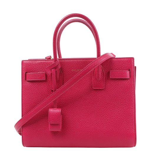 Front view of the Saint Laurent Paris Sac de Jour Baby handbag in bright pink grained leather, featuring dual top handles, a detachable shoulder strap, and signature padlock detail, displayed on a white background.