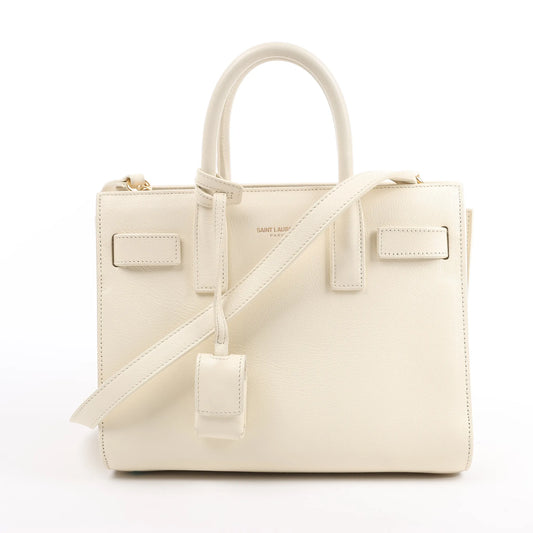 Saint Laurent Paris Sac de Jour Nano handbag in beige grained leather with dual top handles, adjustable and detachable shoulder strap, and signature structured silhouette, displayed against a white background.