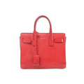 Saint Laurent Sac de Jour Nano red leather structured handbag with top handles, hanging clochette, and gold logo text on front, on white background