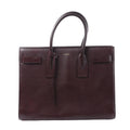 Saint Laurent Sac de Jour handbag in burgundy leather with rolled top handles, structured rectangular shape and belted side details.