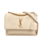 Front view of a beige Saint Laurent Sunset Medium shoulder bag with a suede flap, gold YSL logo, gold chain strap with a beige leather shoulder pad, and smooth leather body on a white background.