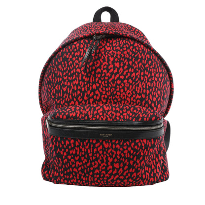 Saint Laurent Paris Leopard Hunting Backpack in red and black canvas with leopard print, black leather trim, front zip pocket, and top handle, shown standing against a white background.