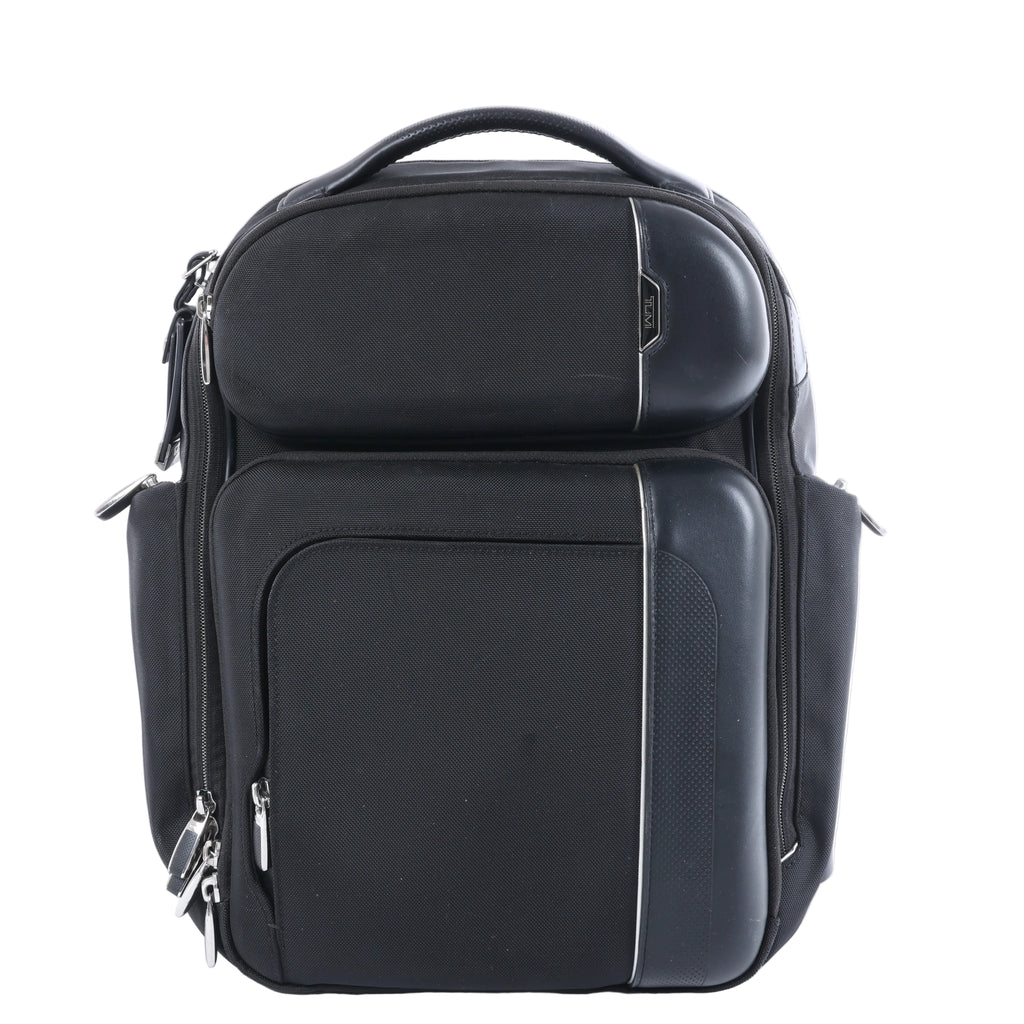 Tumi Arrivé Barker black fabric backpack with multiple front zip compartments, structured black trim, silver-tone zippers and top carry handle.