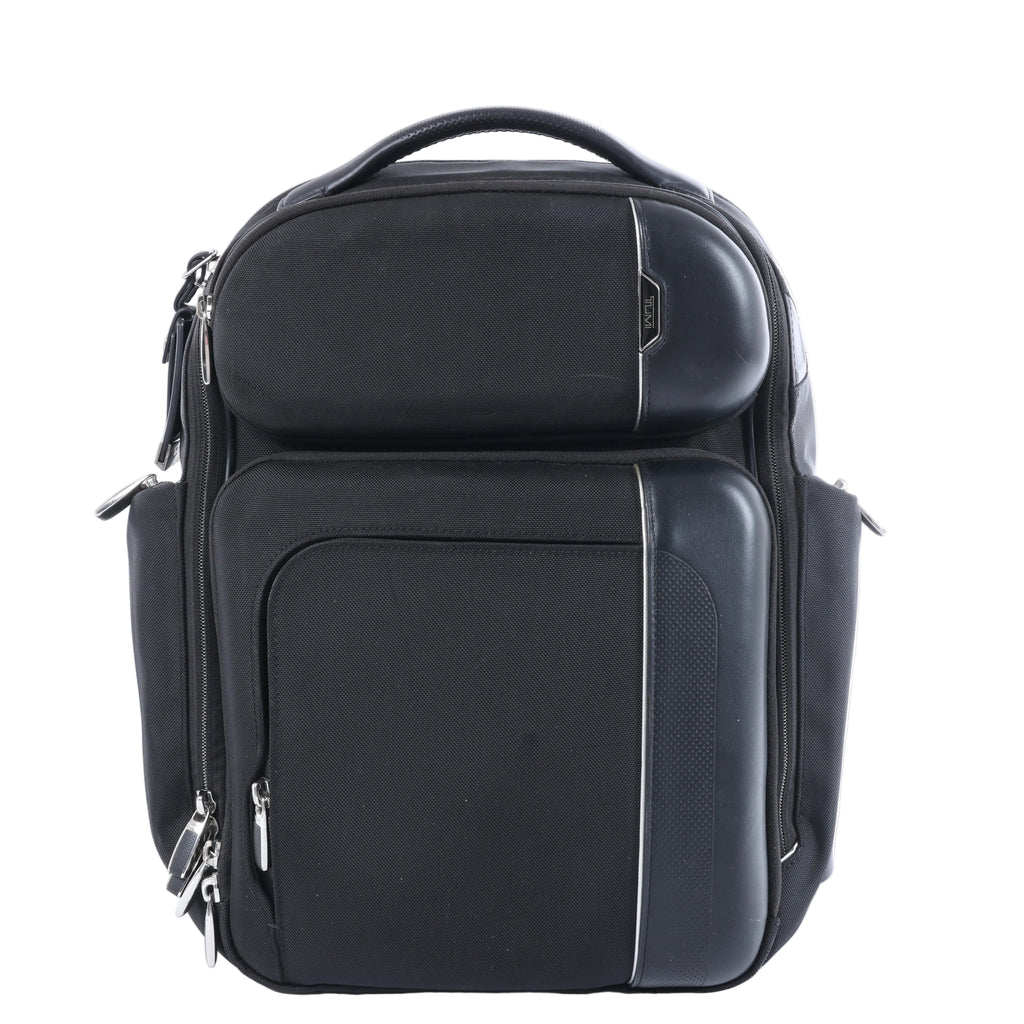 Tumi Arrivé Barker black fabric backpack with multiple front zip compartments, structured black trim, silver-tone zippers and top carry handle.