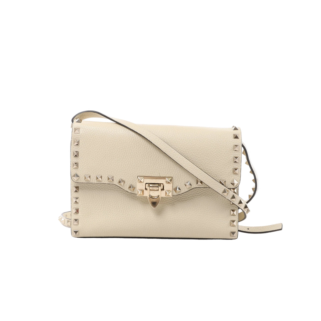 Beige Valentino Garavani Rockstud crossbody bag with grainy leather, pyramid studs, front flap, metal clasp and slender shoulder strap.