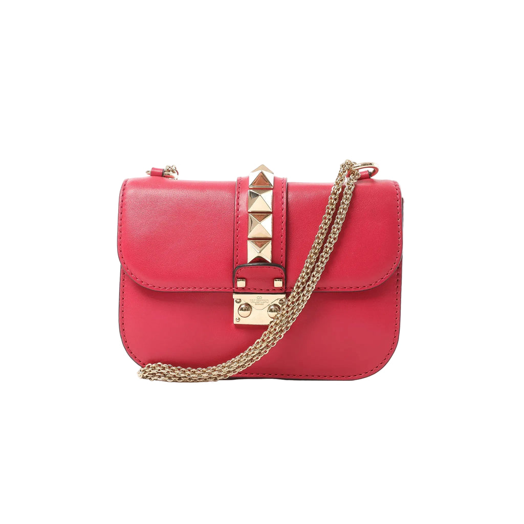Pink Valentino Rockstud Glam Lock leather crossbody bag with gold-tone pyramid stud strap, front lock closure, and gold chain strap on white background.