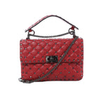 Valentino Rockstud Spike red quilted leather crossbody bag with black-tone studs, chain strap, top handle, and front turn-lock closure on white background.