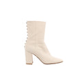 Side view of a Valentino Garavani ivory leather boot with a pointed toe, tall block heel and a row of metallic pyramid studs along the back.