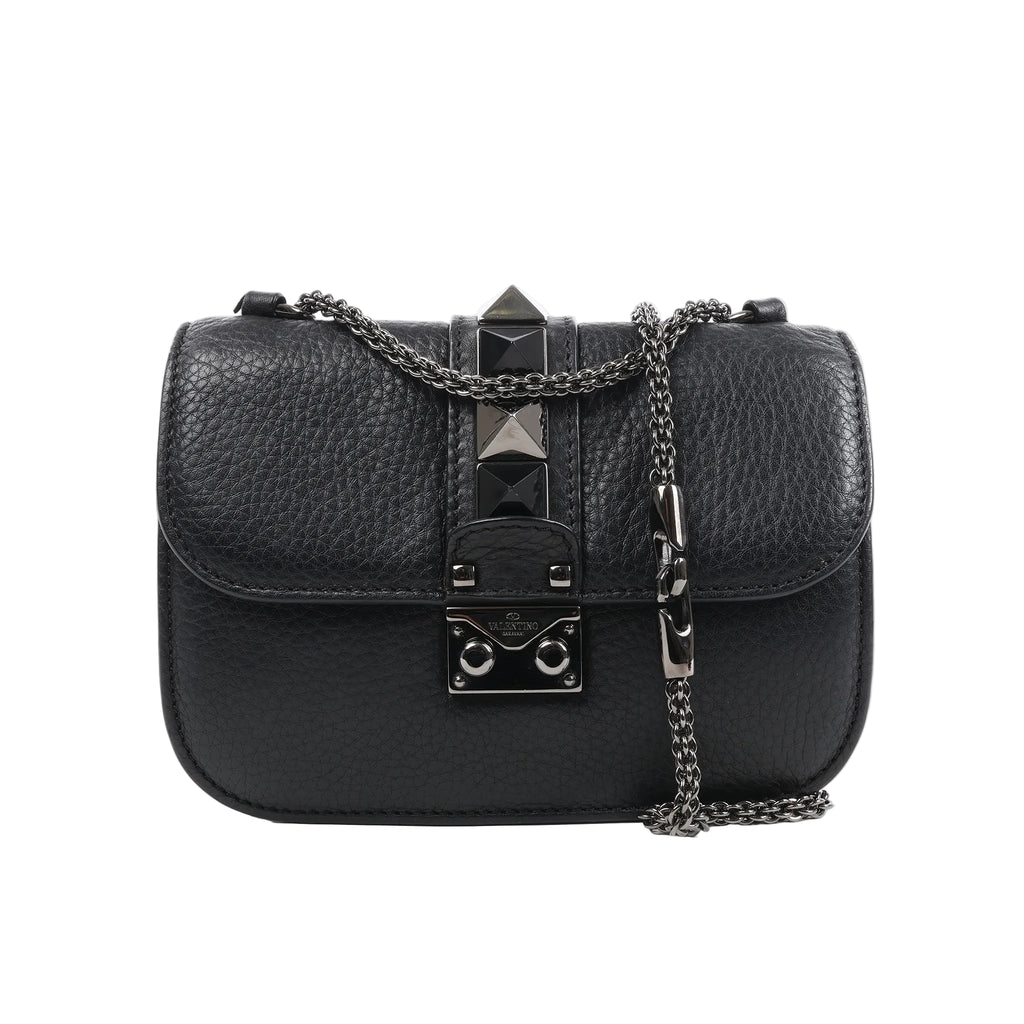 Valentino Rockstud Glam Lock shoulder bag in black grained leather with pyramid stud accents, flap closure with metal lock, and silver-tone chain strap against a white background.