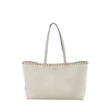 Valentino Garavani Rockstud ecru grained leather shoulder bag with slim shoulder straps, silver-tone stud trim, and structured open-top silhouette on white background.