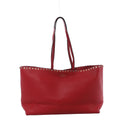 Valentino Garavani Rockstud red grained leather shoulder bag with slim shoulder straps, gold-tone stud trim, and structured open-top tote silhouette on white background.