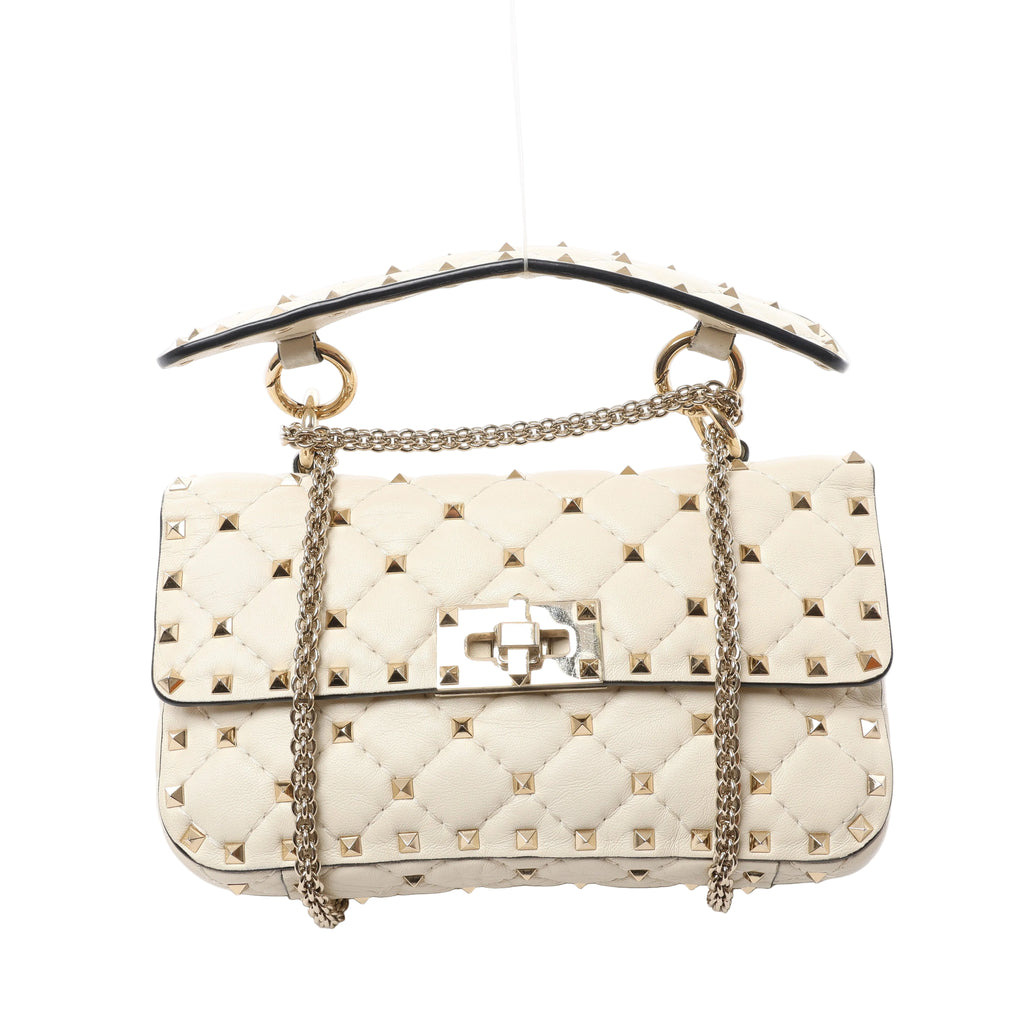 Front view of a beige quilted Valentino Garavani bag with gold-tone pyramid studs, a studded top handle, chain shoulder strap and rectangular turn-lock.