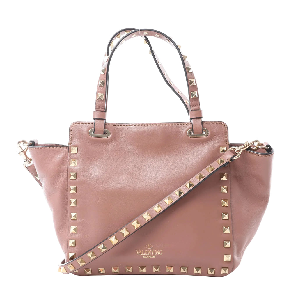 Valentino Garavani Rockstud handbag in dusty pink leather with gold-tone pyramid studs, dual top handles, detachable shoulder strap and gold logo, displayed against a white background.