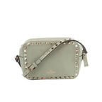Sage green leather Valentino Garavani crossbody bag with gold-tone pyramid studs around the edge, adjustable strap, and zip-top closure on a white background.