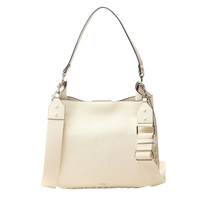 Front view of Valentino Garavani Rockstud Leather Shoulder Bag in ecru grained leather with tonal pyramid stud trim, top handle, and wide adjustable shoulder strap, displayed against a white background.