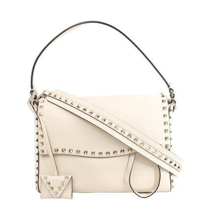 Valentino Garavani Rockstud 2Way Handbag in beige leather featuring signature gold-tone pyramid studs along the edges and strap, with a top handle, detachable shoulder strap, and matching studded coin pouch.