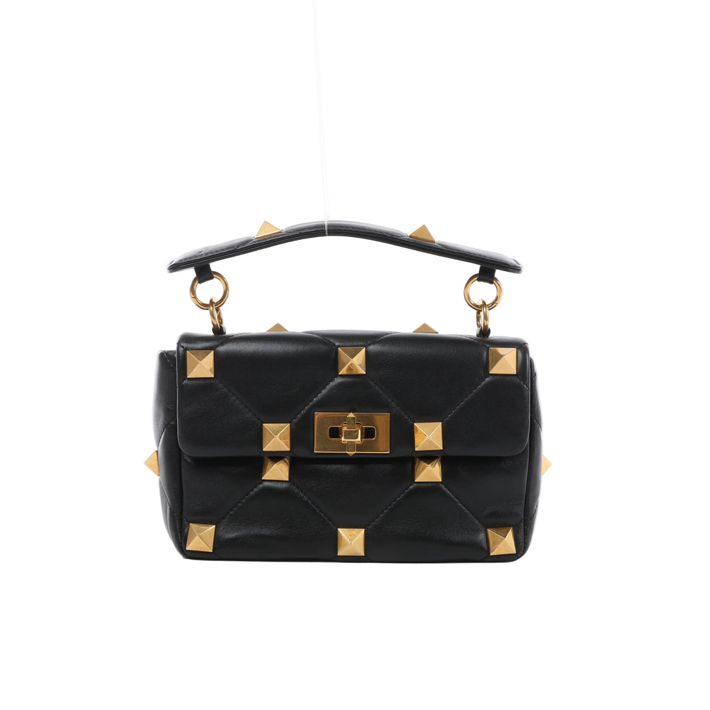 Front view of Valentino Garavani black quilted leather handbag with oversized gold-tone pyramid studs, a studded top handle and turn-lock flap closure.