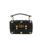 Front view of Valentino Garavani black quilted leather handbag with oversized gold-tone pyramid studs, a studded top handle and turn-lock flap closure.
