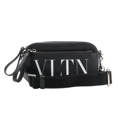 Front view of the Valentino Garavani VLTN Leather Shoulder Bag in black, featuring smooth leather exterior, bold white VLTN logo print, front zip pocket, detachable black fabric strap, and silver-tone hardware, displayed against a white background.