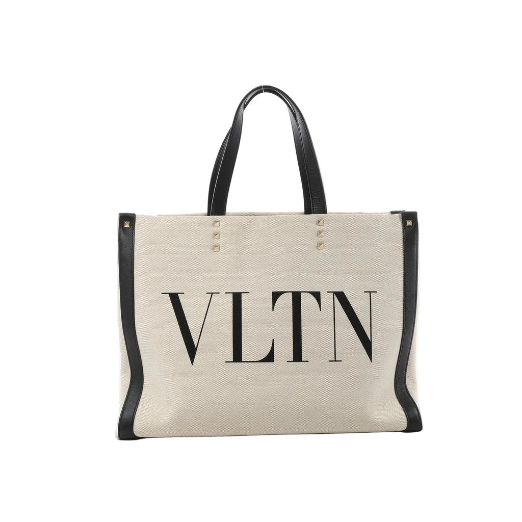 Valentino Garavani VLTN beige canvas tote bag with black leather trim, black top handles, stud details, and large black VLTN logo print on the front.
