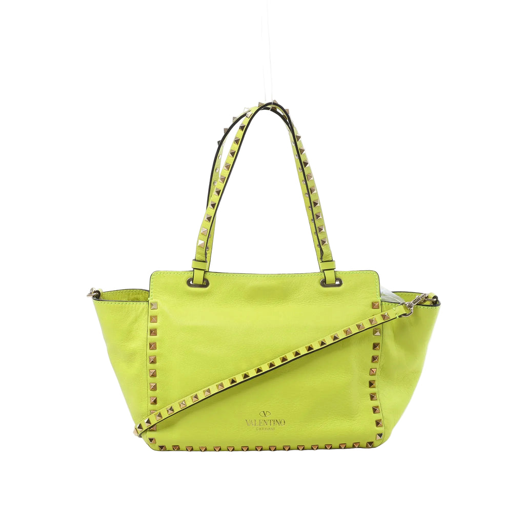 Valentino Garavani Rockstud yellow leather 2-way handbag with gold-tone pyramid studs, double top handles, and detachable shoulder strap on white background