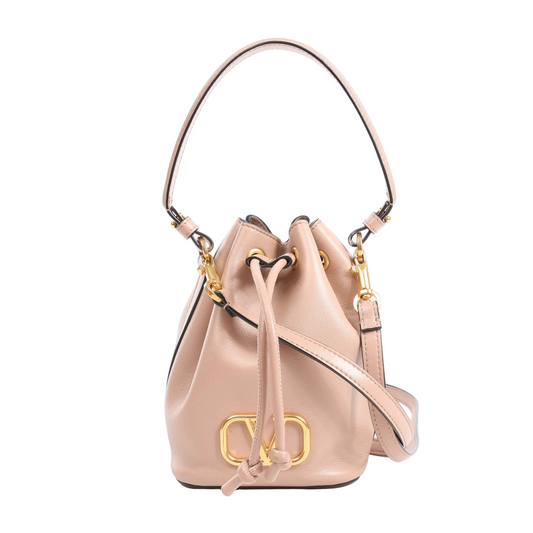 Front view of the Valentino Garavani Buckets 2Way Shoulder Bag in powder pink leather with gold-tone VLogo hardware, drawstring closure, top handle, and detachable shoulder strap, displayed on a white background.