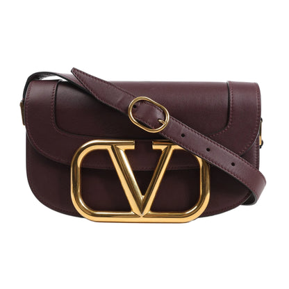 Valentino Garavani Supervee Shoulder Bag in burgundy leather featuring a large gold VLogo buckle on the front flap, adjustable matching leather strap with gold hardware, and structured silhouette, displayed on a white background.