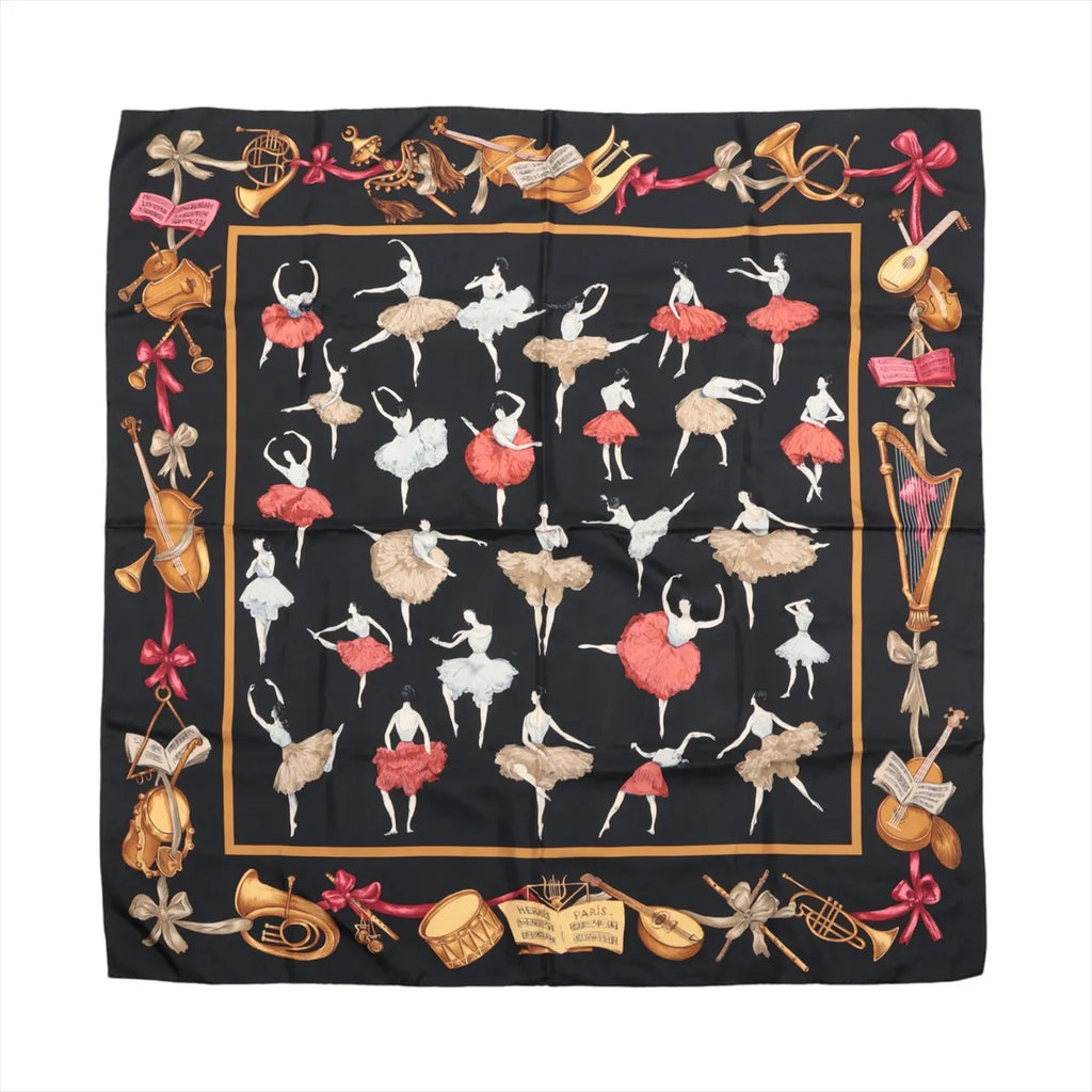 Black Hermès Carré 90 scarf laid flat with red and white ballerinas, musical sheets, pointe shoes and colourful ballet-themed border motifs.