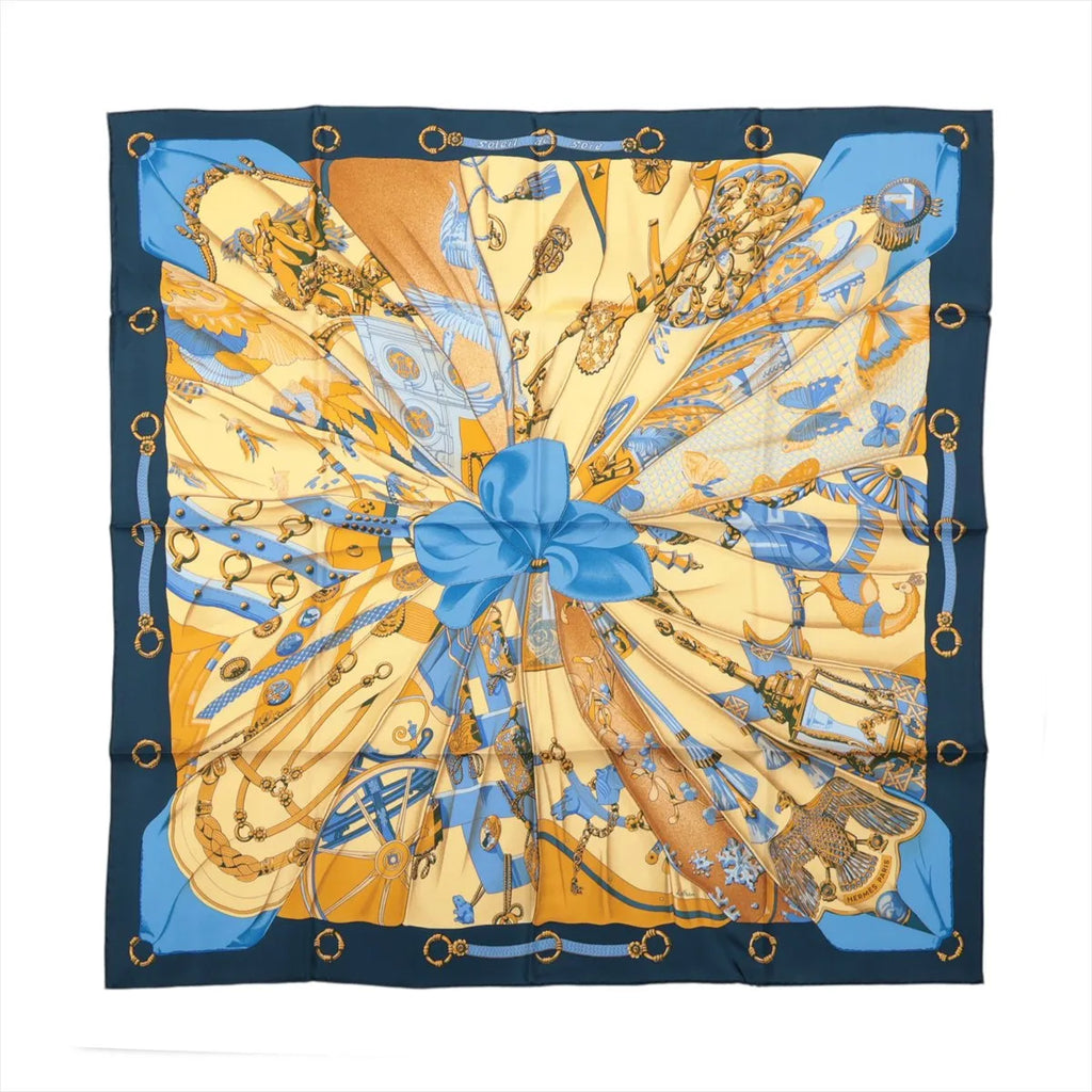 Hermès Carré 90 Soleil de Soie silk scarf with navy border, gold background, blue central bow and detailed equestrian motifs.