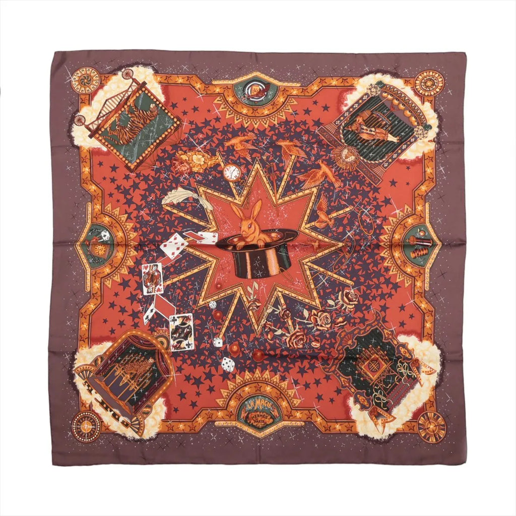 Hermès Carré 90 La Magie silk scarf in brown and red with rabbit in magician’s hat, playing cards, stars, birds and ornate gold motifs.