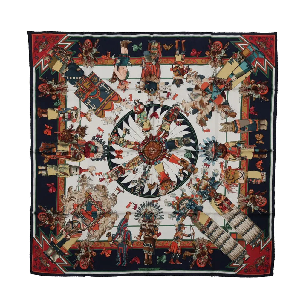Hermès Kachinas silk scarf with navy blue border, colorful ceremonial figures, feathered headdresses and red, green and cream geometric motifs.